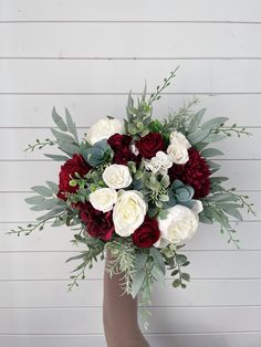 a bouquet of red and white flowers in a vase with greenery on the side