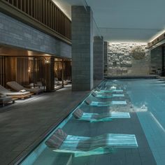 an indoor swimming pool with chaise lounges next to it and large windows on the side