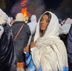 a woman wrapped up in a blanket standing next to a group of people near a fire