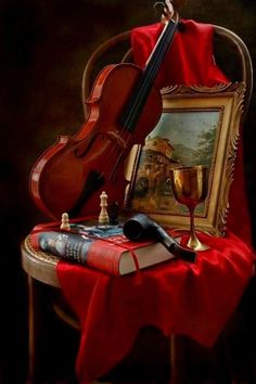 a violin sitting on top of a table next to a wine glass and book with a painting in the background