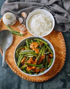 two bowls filled with green beans and rice next to spoons on a wooden tray