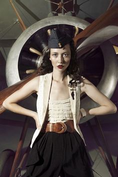 a woman standing in front of an airplane with her hands on her hips and wearing a hat