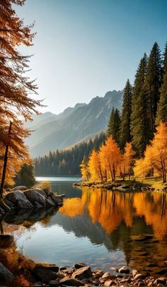 a lake surrounded by trees with yellow leaves on the water and mountains in the background