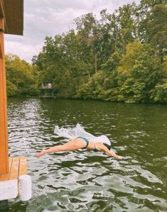 a woman floating on top of a body of water next to a wooden dock with trees in the background