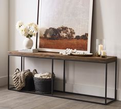 a wooden table with baskets and candles on it next to a large framed photograph in the corner