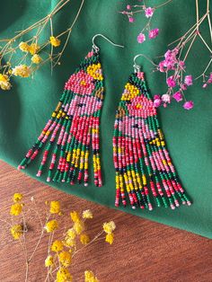 two pairs of colorful beaded earrings sitting on top of a green cloth next to flowers