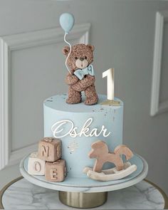 a blue cake with a teddy bear on top and wooden blocks in the shape of numbers