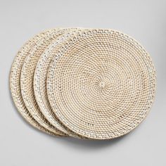 three round woven placemats on a gray surface with one white and the other beige