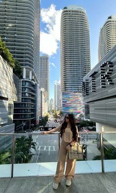 a woman standing in front of tall buildings with her hand on the railing and looking at the camera