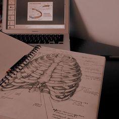 an open laptop computer sitting on top of a desk next to a drawing book and pencil