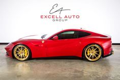 a red sports car with gold rims parked in front of a sign that says excel auto group