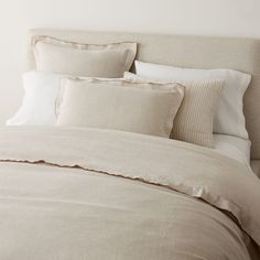 an unmade bed with beige linens and pillows