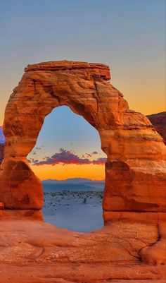 an arch shaped rock formation in the desert at sunset with clouds and mountains in the background