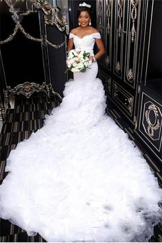 a woman in a white wedding dress standing next to a black cabinet and holding a bouquet