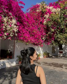 a woman is standing in front of some pink and white bougaia trees with her back to the camera