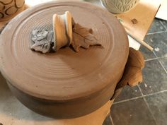 a clay pot sitting on top of a table next to two vases with leaves