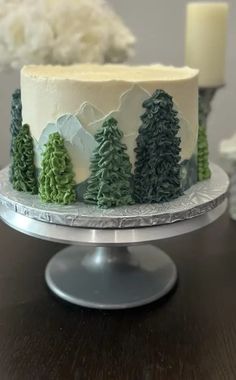 a cake decorated with trees and frosting on top of a wooden table next to two candles