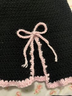 a crocheted black and pink dress with a bow on the front, sitting on a bed