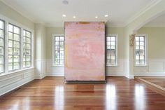 an empty room with wood floors and large pink painting on the wall in front of two windows