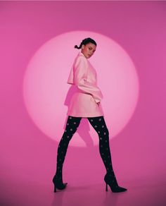 a woman in a pink coat and polka dot patterned tights poses for a photo