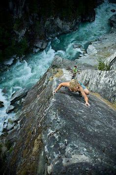 a woman climbing up the side of a cliff next to a river