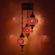 three colorful lights hanging from a chain in a room with red and yellow light shining on the wall