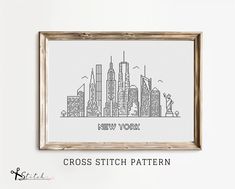 a cross stitch city skyline is displayed in a wooden frame on a white wall with the words new york written across it