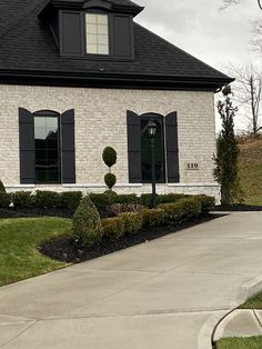 a white brick house with black shutters on the windows and bushes in front of it