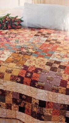 a bed with a quilt on top of it next to a pillow and flower arrangement