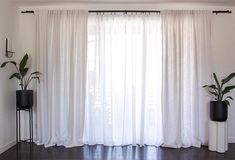 a living room with white curtains and black planters