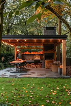 an outdoor kitchen is lit up by string lights and surrounded by trees with leaves on the ground