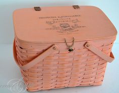 an antique pink wicker picnic basket with leather handles and strap closures on the front