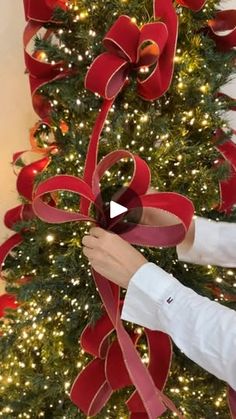 a woman is decorating a christmas tree with red ribbon