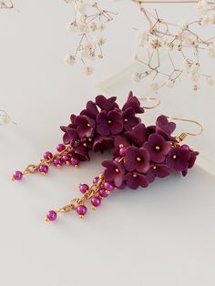 purple flowers and pearls hang from gold - plated earwires on a white surface