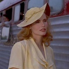 a woman standing in front of a train with a hat on her head and looking off to the side