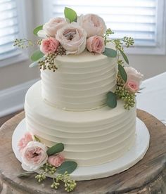 a three tiered cake with flowers and greenery on the top is sitting on a wooden table