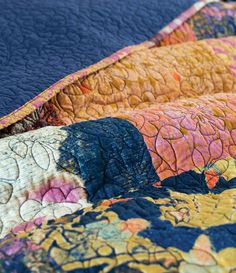 a close up of a quilt on a bed with blue and yellow sheets in the background