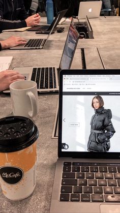 two laptops and a coffee cup on a table with people sitting at tables in the background