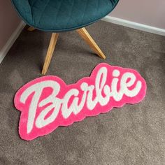 a pink rug with the word barbie on it in front of a blue chair and green chair