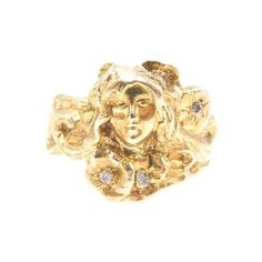 a gold ring with a woman's face and flowers on the front, set against a white background