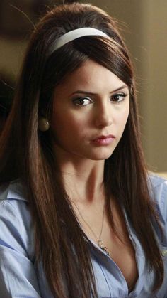 a woman with long hair wearing a blue shirt and white headband looking at the camera