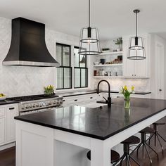 a large kitchen with an island and black counter tops in the center, surrounded by white cabinets