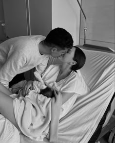 a man kissing a woman on the cheek in a hospital bed while she is holding her baby