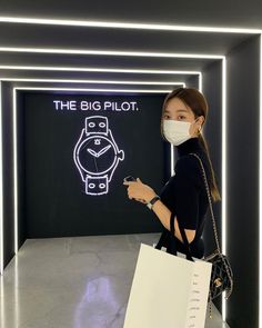 a woman wearing a face mask standing in front of a sign that says the big pilot