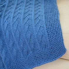 a blue knitted blanket sitting on top of a white couch next to a pillow