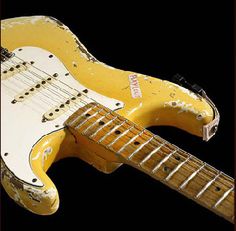 an old yellow electric guitar sitting on top of a black background