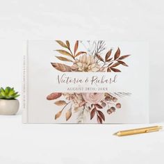 a wedding guest book with watercolor flowers on it next to a pen and succulent