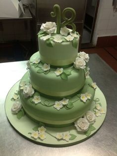 a three tiered green cake with white flowers on the bottom and number twelve on top