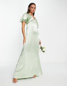 a woman in a long green dress holding a white bouquet and posing for the camera