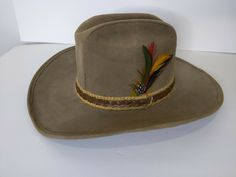 Preowned United Hatters Cap & Millinery Workers Large Tan Felt Cowboy Western Country Hat Size Large  Brown braid and jute band Green, red yellow and brown feather decor Top Hat For Kentucky Derby And Country Events, Country Style Brimmed Top Hat, One Size, Fitted Short Brim Costume Hat For Country Events, Country Style Brimmed Top Hat, Fitted Brimmed Mini Hats For Country Events, Western Style Kentucky Derby Costume Hat With Short Brim, Western Mini Hat With Short Brim, Vintage Felt Hat For Country Events, Western Style Mini Hat With Short Brim